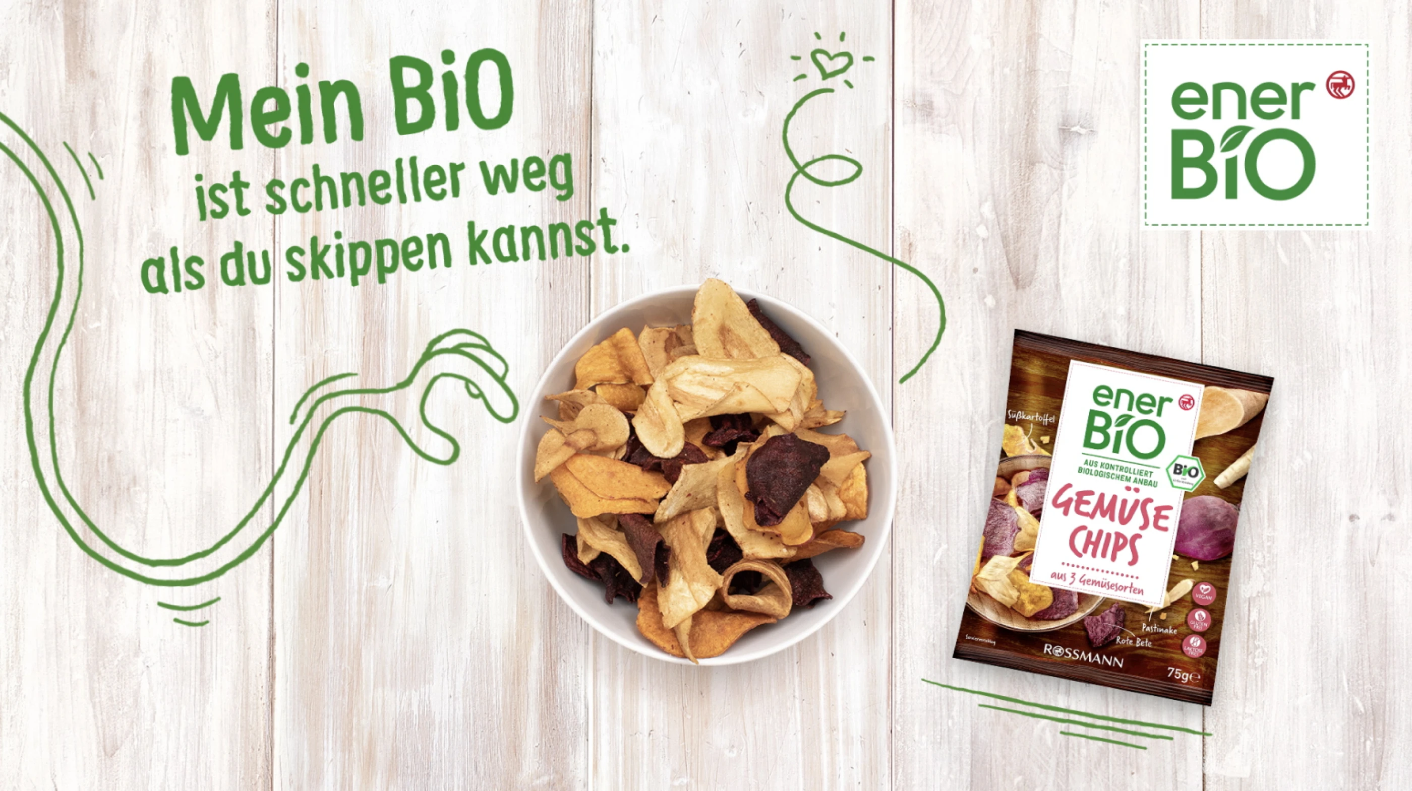 Ein Schalen voller Gemüsechips liegt auf einem hellen Holztisch. Daneben befindet ein Text "Mein Bio ist schneller weg als du skippen kannst.", eine Packung mit dem Aufdruck "enerBIO Gemüse Chips" und grüne, schwungvolle Linien Illustrationen.